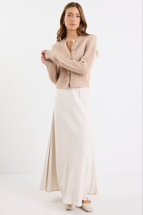 Woman wearing a beige cardigan and white dress on a white background