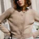Woman wearing a beige cardigan standing outdoors with classical architecture in the background