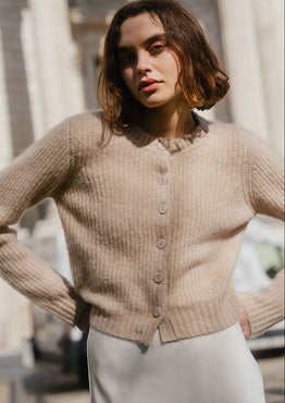 Woman wearing a beige cardigan standing outdoors with classical architecture in the background