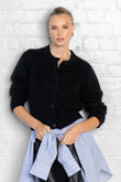Woman wearing a black cardigan over a blue shirt against a white brick wall