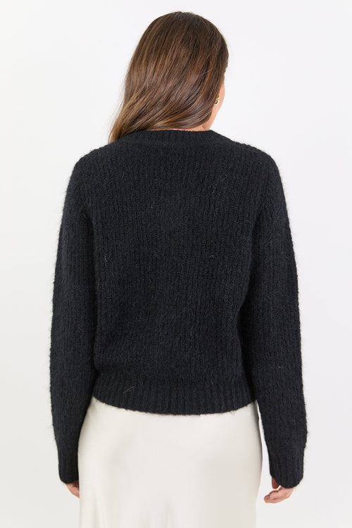 Person wearing a black sweater and white skirt on a plain background