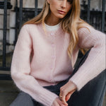Woman wearing a pink sweater sitting against a black metal gate.