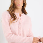 Woman wearing a light pink sweater and blue jeans against a white background