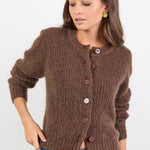 Woman wearing a brown knitted cardigan and blue jeans on a white background