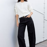 Woman in a white shirt and black pants standing against a modern architectural wall.