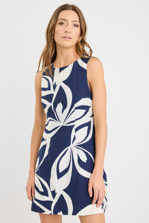 Woman wearing a navy sleeveless mini dress with a bold cream abstract print, styled simply with natural makeup and soft waves.