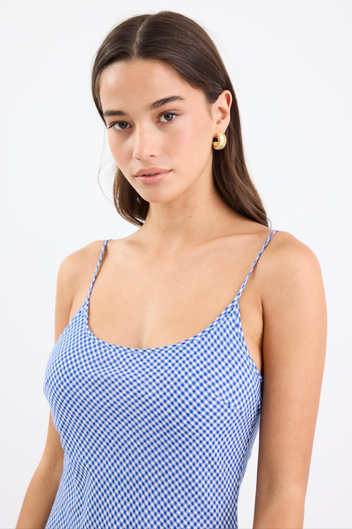 Model wearing a mini gingham strappy slip dress in electric blue, with adjustable straps and a flattering bias cut.
