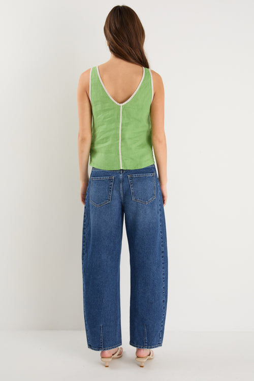 the model wears a green v-neck tank top with dark blue jeans