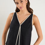 Woman wearing a sleeveless black linen top with contrast beige trim, styled with relaxed mid-blue denim jeans.