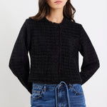 Woman wearing a black textured sweater and blue jeans on a white background