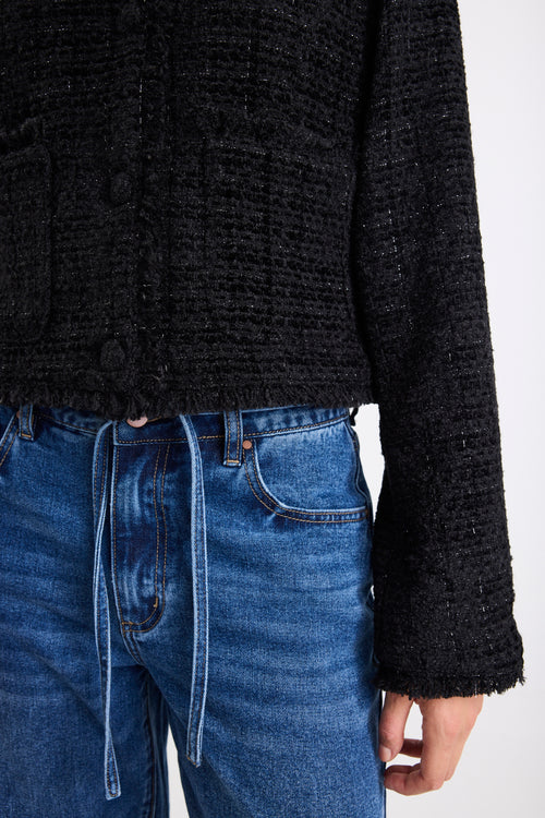 Person wearing a black textured sweater and blue jeans on a white background