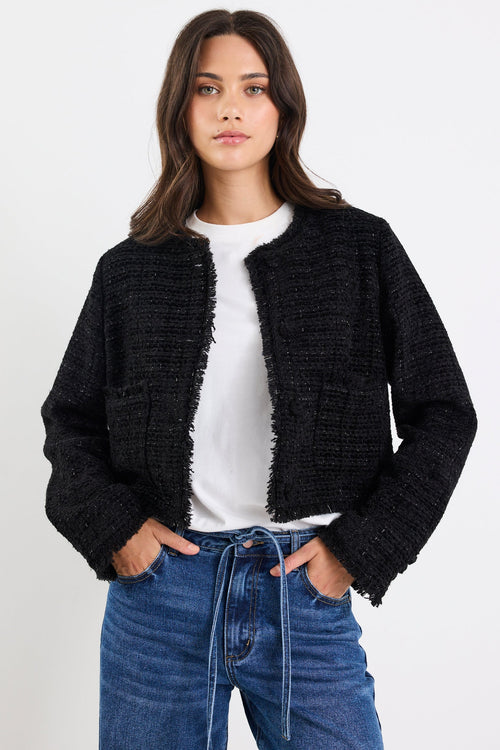 Woman wearing a black textured cardigan over a white shirt and blue jeans on a white background