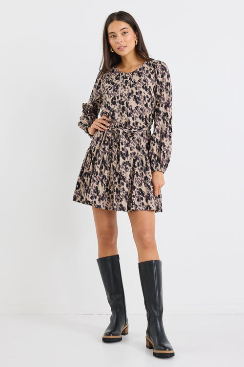 Woman wearing a long-sleeve mini dress with an animal print pattern, belted at the waist with a flared tiered skirt and black boots.