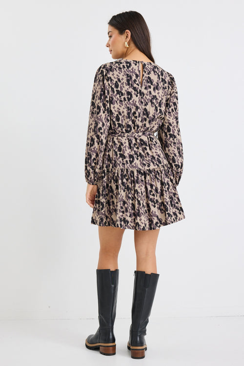 Woman wearing a long-sleeve mini dress with an animal print pattern, belted at the waist with a flared tiered skirt and black boots.