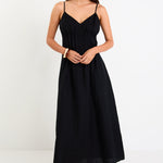 Model wearing a black strappy linen-blend maxi dress with a pleated bodice and an A-line flowing skirt.