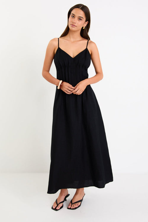 Model wearing a black strappy linen-blend maxi dress with a pleated bodice and an A-line flowing skirt.