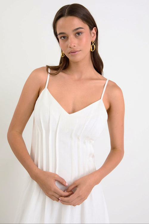 Woman wearing a white dress with gold earrings on a plain background