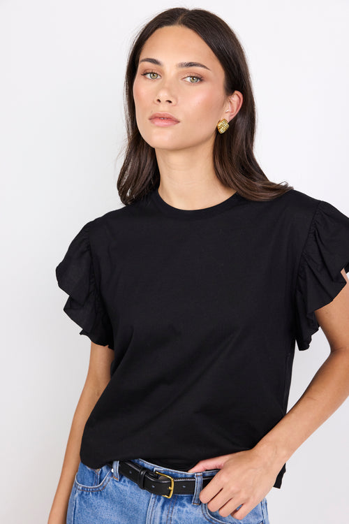 Woman wearing a black top with ruffles on the sleeves and blue jeans on a white background