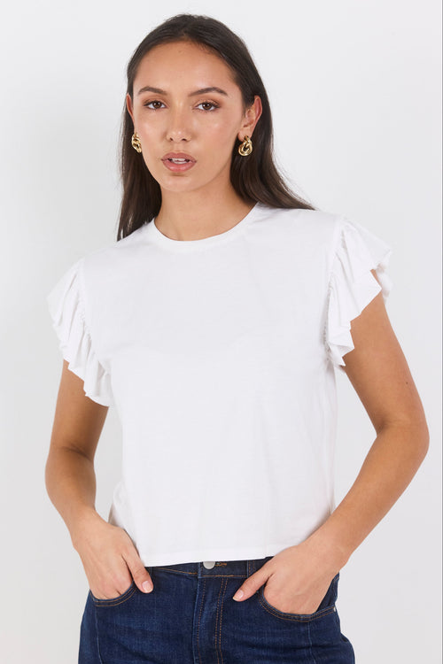 Woman wearing a white ruffled top and dark jeans on a white background