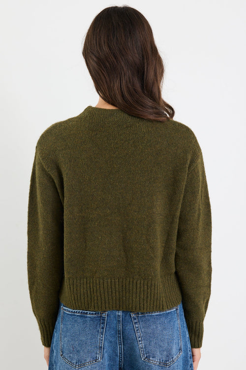 Person wearing a green sweater and blue jeans on a white background