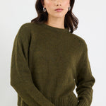 Woman wearing an olive green sweater and blue jeans on a white background