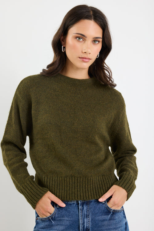 Woman wearing an olive green sweater and blue jeans on a white background