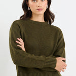 Woman wearing an olive green sweater and blue jeans against a white background