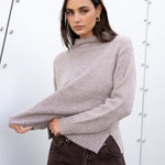 Woman wearing a gray sweater and dark jeans against a white background