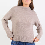 Woman wearing a beige sweater and blue jeans on a white background
