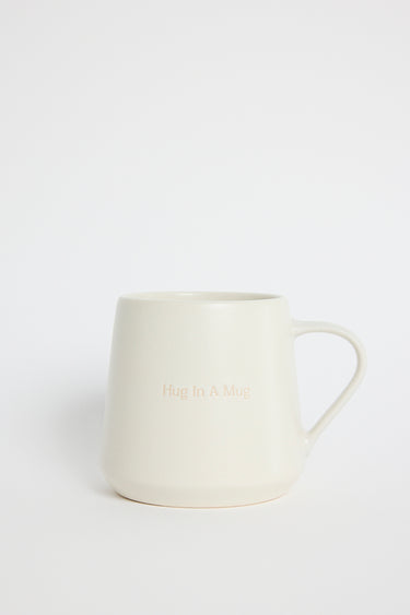 Cream-coloured ceramic mug with the words ‘Hug In A Mug’ embossed on the front, photographed on a white background
