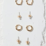 Set of gold earrings on a white stone display block against a beige background