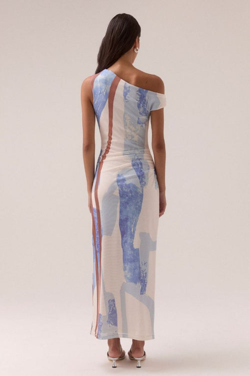 One-shoulder mesh maxi dress with vertical abstract stripes in blue, rust, and cream tones, featuring a fitted silhouette and side ruching, worn by a model in white sandals against a neutral background.