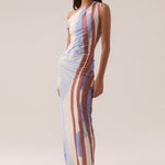 One-shoulder mesh maxi dress with vertical abstract stripes in blue, rust, and cream tones, featuring a fitted silhouette and side ruching, worn by a model in white sandals against a neutral background.