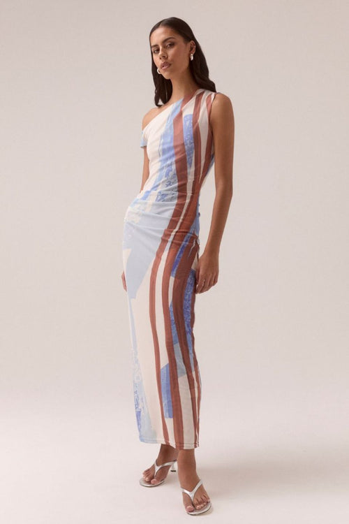 One-shoulder mesh maxi dress with vertical abstract stripes in blue, rust, and cream tones, featuring a fitted silhouette and side ruching, worn by a model in white sandals against a neutral background.