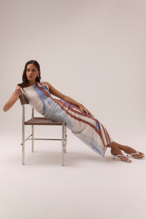 One-shoulder mesh maxi dress with vertical abstract stripes in blue, rust, and cream tones, featuring a fitted silhouette and side ruching, worn by a model in white sandals against a neutral background.