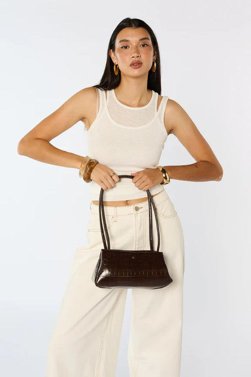 Woman holding a brown handbag against a white background