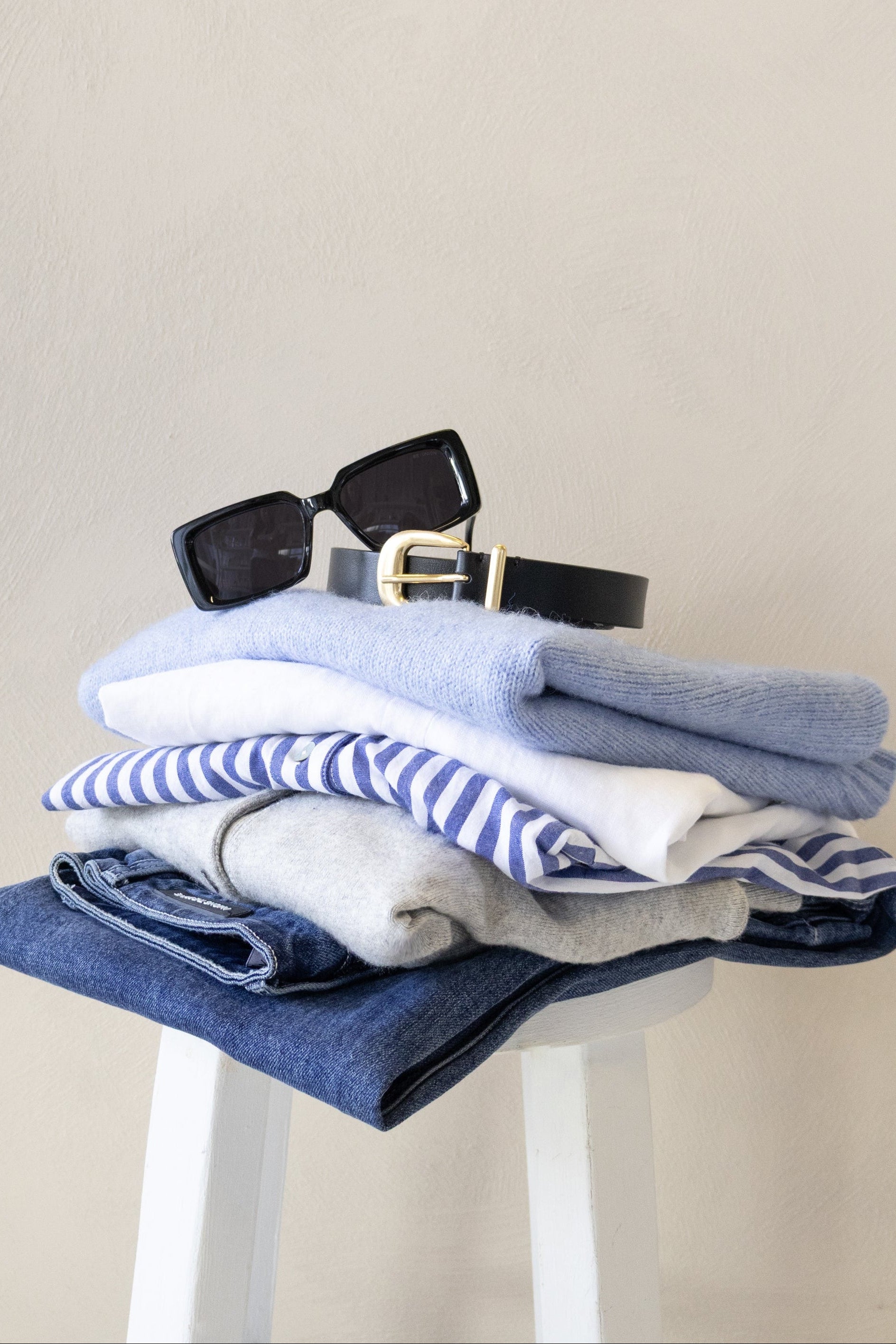 Stack of folded clothes on a white stool against a beige wall