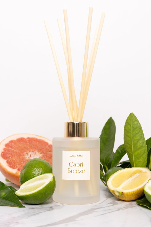 Reed diffuser labeled 'Capri Breeze' with citrus fruits and leaves on a white background