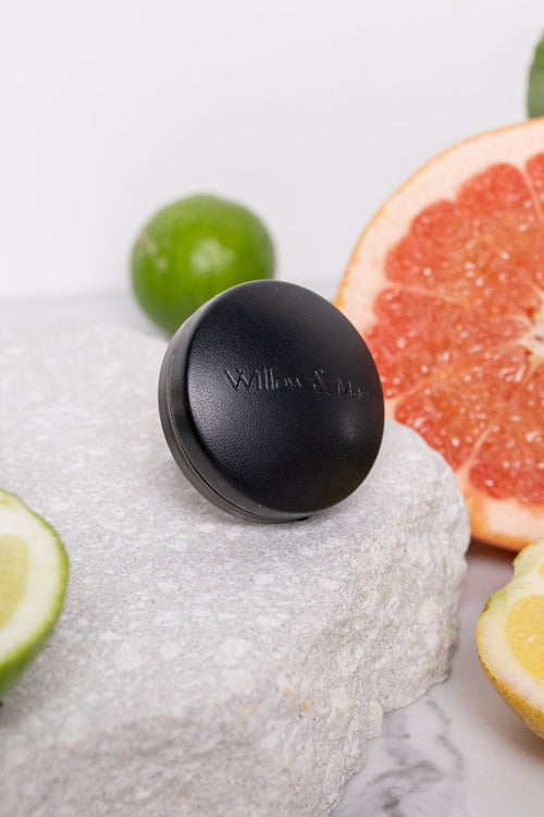 Black soap bar on a marble surface with sliced limes, lemons, and a grapefruit.