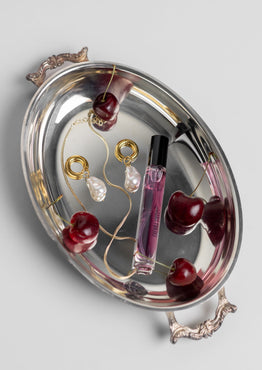 Silver tray with jewelry and cherry decorations on a light gray background