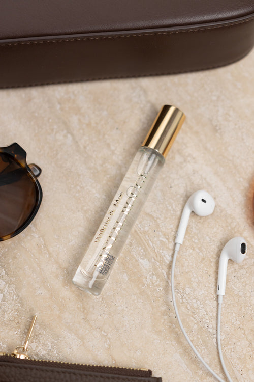Clear spray bottle with gold cap, sunglasses, earphones, and wallet on a beige surface