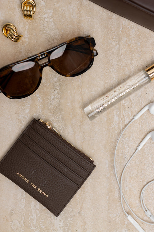 Brown cardholder, sunglasses, and earphones on a beige surface