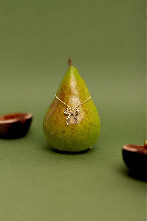 Gold necklace with a pendant on a green pear against a green background