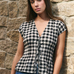 Woman wearing a black and white checkered top against a stone wall