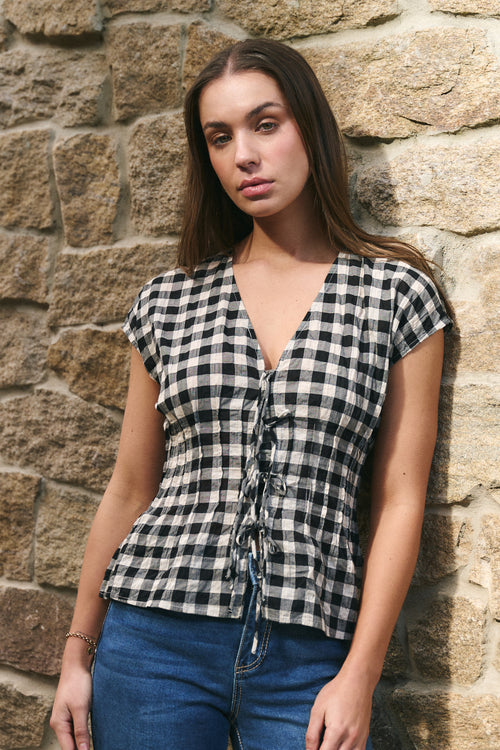 Woman wearing a black and white checkered top against a stone wall