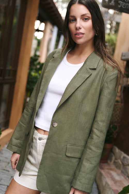 Woman wearing a green blazer over a white top and shorts outdoors.
