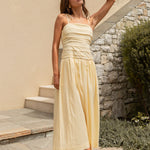 Woman in a yellow dress standing outdoors near a building with stone walls.