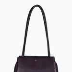 A dark chocolate leather shoulder bag with a single long strap and a small gold logo on the front, set against a plain white background.