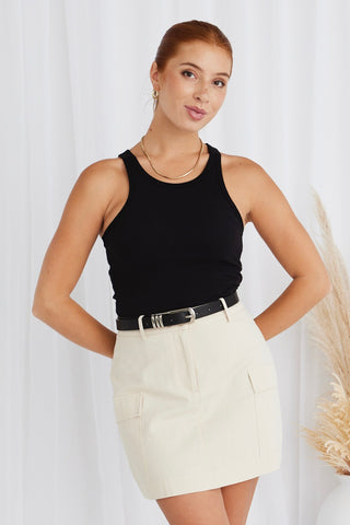 model wears a cream mini skirt and black tank top