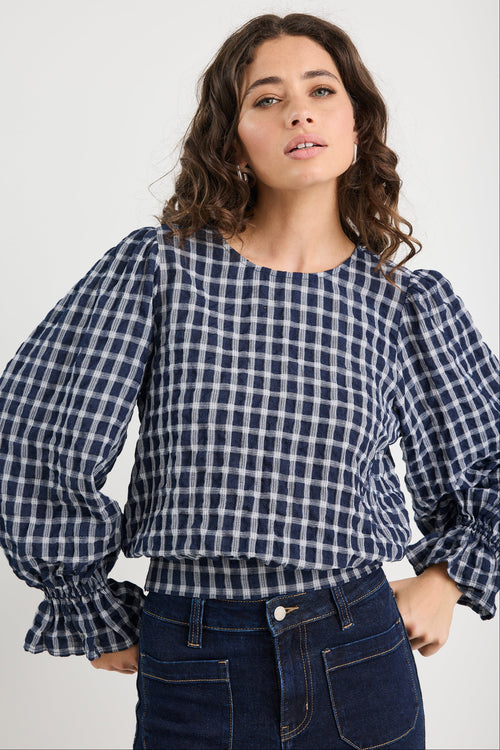 Woman wearing a blue and white checkered blouse with puffed sleeves on a plain background